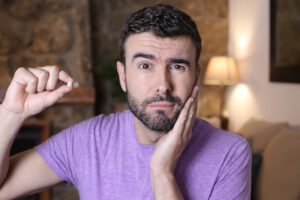 man in a purple shirt suffering from jaw pain holding up a piece of a chipped tooth in his right hand