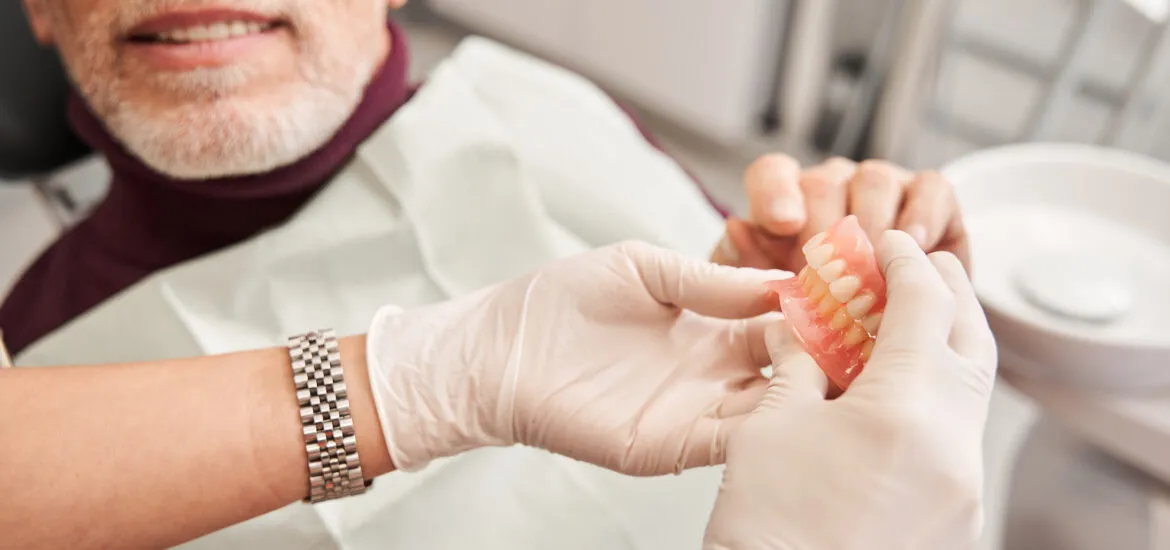 doctor showing a pair of dentures to a older male patient