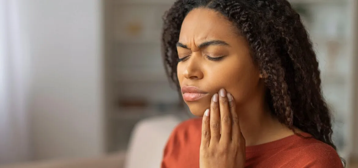 woman in a red sweater with her hand on her jaw, suffering from severe tooth pain