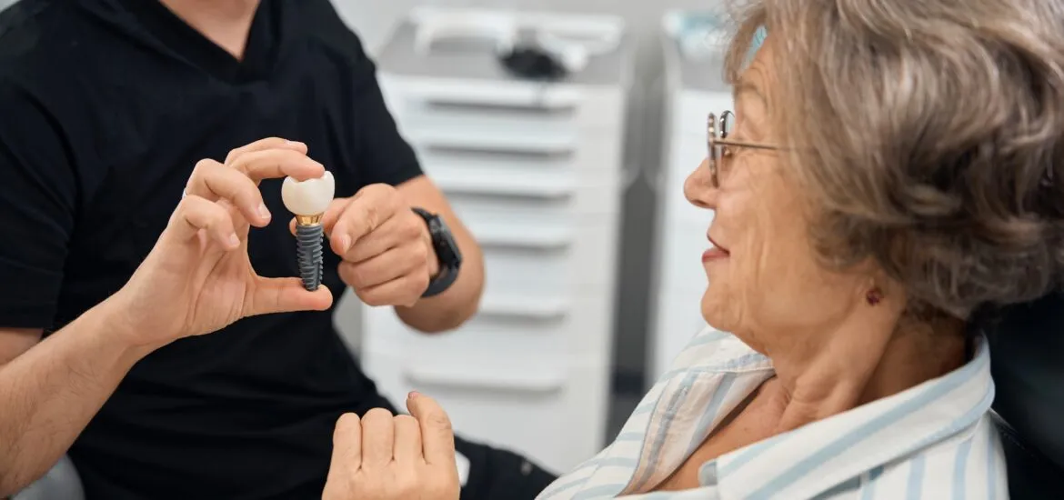 Patient examines model of dental implant in hands of dentist