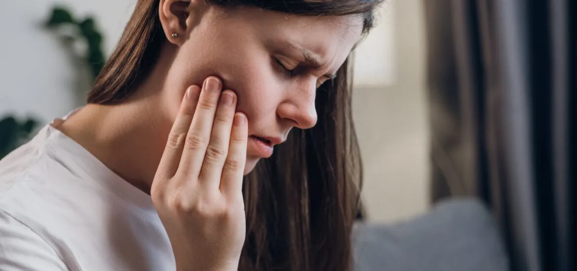 young woman sitting on couch with her hand in jaw, wisdom tooth pain