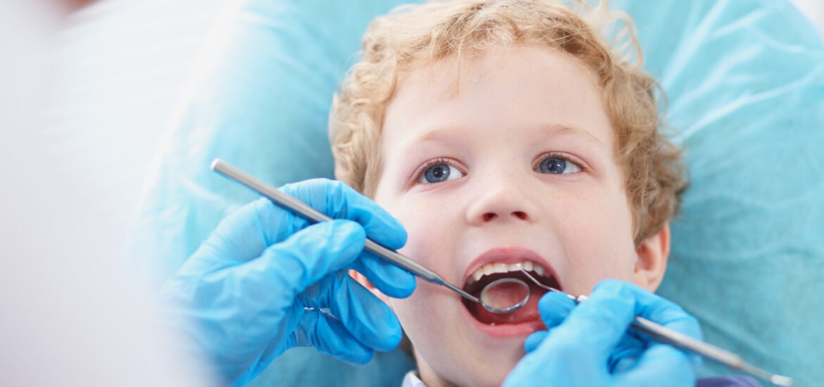 little boy having his teeth examined by a doctor in blue gloves